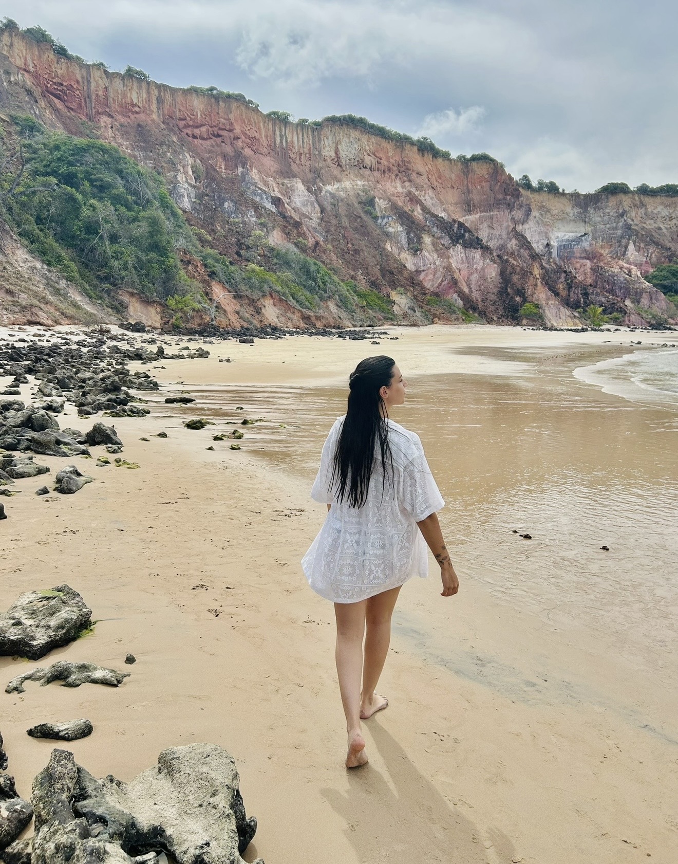 Gabrielly Christinne caminhando pela praia, de costas, em um cenário tranquilo